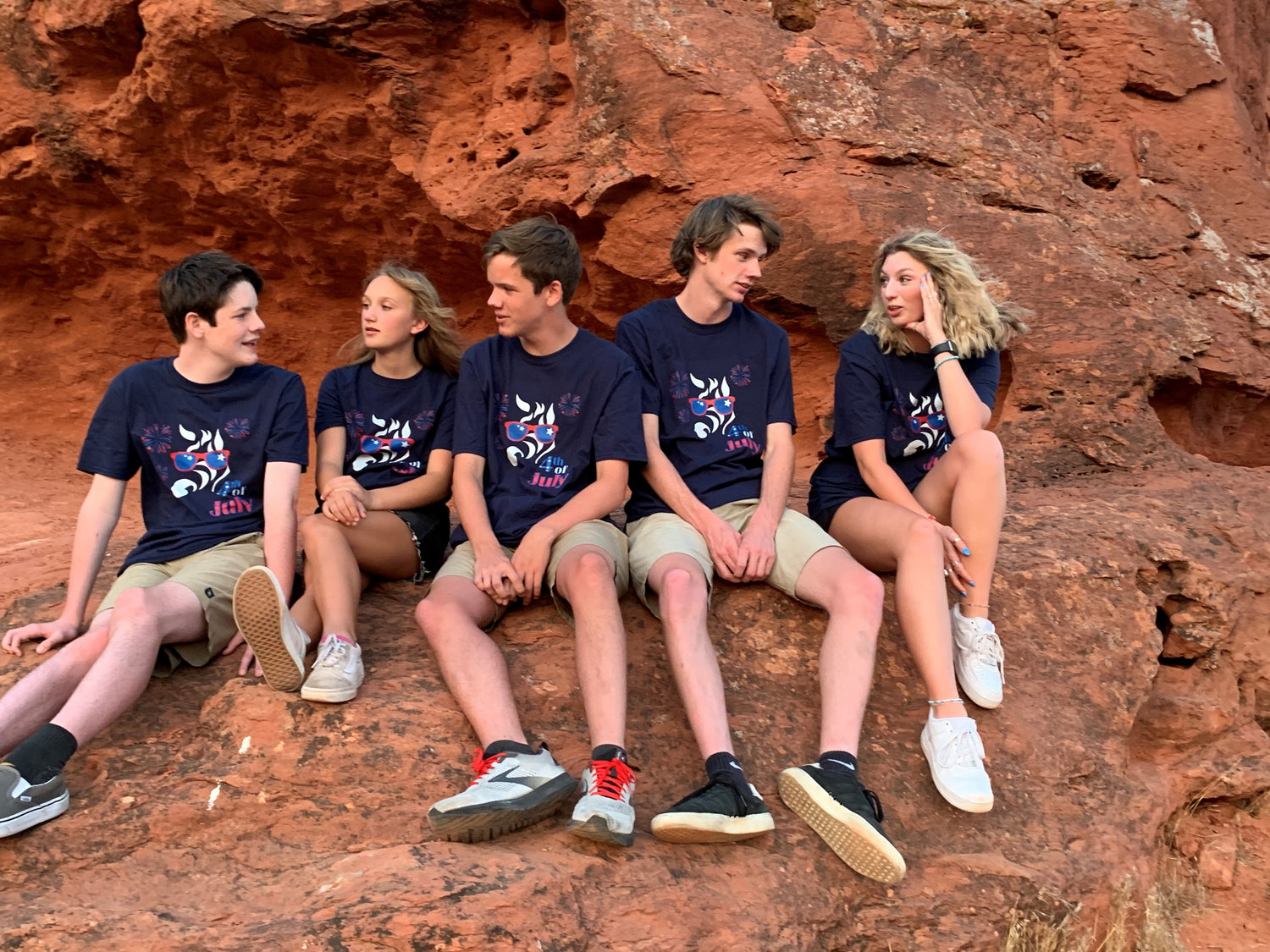 Group of people wearing matching navy graphic unisex t-shirts sitting together on red rock terrain outdoors
