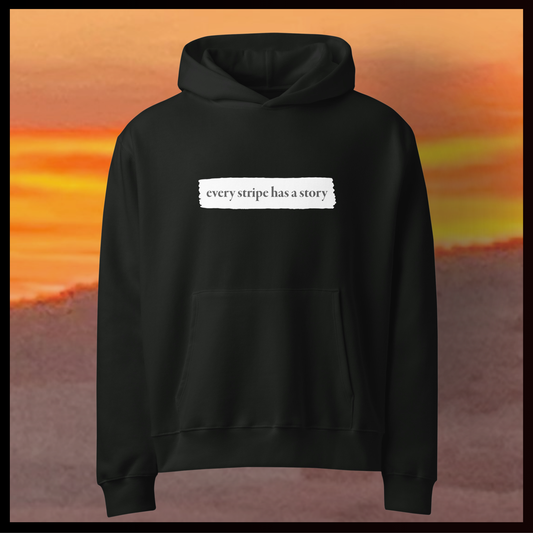 Black hoodie with text 'every stripe has a story' against a sunset background